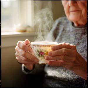 Flux 2 output for the prompt: A 35mm film photo of an elderly woman's hands holding a steaming porcelain teacup, natural window light, Portra 400 grain