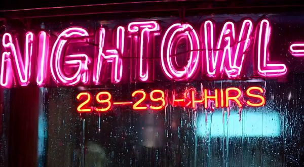 Wan v2.2 output for the prompt: Extreme close-up of a neon diner sign flickering on that reads "NIGHT OWL — 24 HRS" in pink and yellow tubes, rain streaming down the glass behind it. 1990s aesthetic.