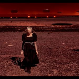 Add UFOs in the sky, change the woman's dress to a black emo one, make her look old, and set the scene in a sci-fi atmosphere like the movie War of the Worlds.