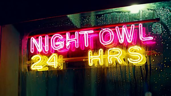 Minimax output for the prompt: Extreme close-up of a neon diner sign flickering on that reads "NIGHT OWL — 24 HRS" in pink and yellow tubes, rain streaming down the glass behind it. 1990s aesthetic.