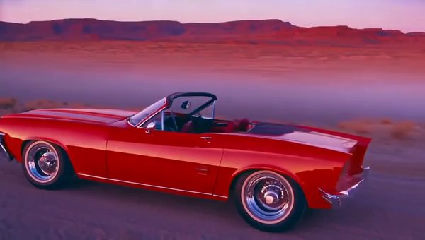 Mochi output for the prompt: Slow orbit around a 1965 Mustang convertible parked on a Nevada desert highway at twilight. Neon motel sign blinking in the background. Cinematic widescreen.