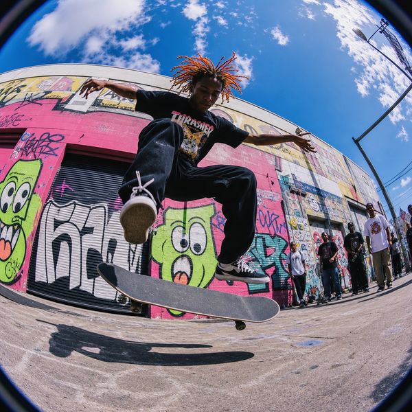High-energy wide-angle street photography style with extreme fisheye distortion shot from low angle, featuring direct harsh sunlight creating sharp shadows and saturated neon colors—electric blues, hot pinks, lime greens—with intense contrast. Figures in spontaneous motion with slight blur against concrete and graffitied urban surfaces. Candid youth culture and street fashion moments captured raw and visceral, emphasizing dynamic energy and attitude. Generate random, unpredictable scenes each time.