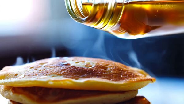 Minimax output for the prompt: A slow-motion close-up of honey being poured from a glass jar onto warm pancakes, light catching the viscous drip, steam rising subtly. Handheld, shallow depth of field.