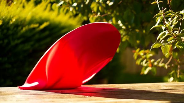 Minimax output for the prompt: A red silk scarf blows off a wooden table in a gentle breeze, drifting in slow motion across a sunlit garden before catching on a rosebush. 50mm lens.