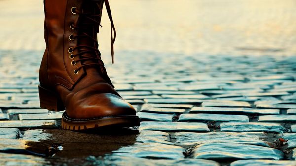 Minimax output for the prompt: A brown leather boot drops into a shallow puddle on a cobblestone street. Water splashes in a perfect circle, then settles. Slow motion 120fps, dawn light.