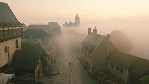 Luma Ray 2 output for the prompt: Aerial crane shot descending over a medieval European village at dawn. Fog clinging to cobblestone streets, a baker pulling bread from a stone oven. Warm golden hour light.