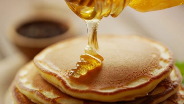 Luma Ray 2 output for the prompt: A slow-motion close-up of honey being poured from a glass jar onto warm pancakes, light catching the viscous drip, steam rising subtly. Handheld, shallow depth of field.