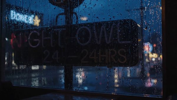 Google Veo 3.1 Lite output for the prompt: Extreme close-up of a neon diner sign flickering on that reads "NIGHT OWL — 24 HRS" in pink and yellow tubes, rain streaming down the glass behind it. 1990s aesthetic.