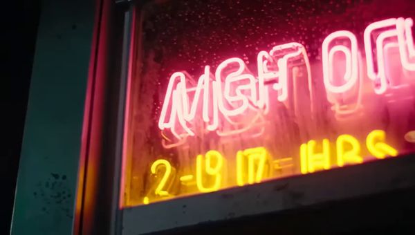 Mochi output for the prompt: Extreme close-up of a neon diner sign flickering on that reads "NIGHT OWL — 24 HRS" in pink and yellow tubes, rain streaming down the glass behind it. 1990s aesthetic.