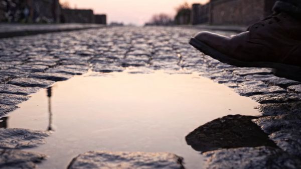 Google Veo 3.1 Lite output for the prompt: A brown leather boot drops into a shallow puddle on a cobblestone street. Water splashes in a perfect circle, then settles. Slow motion 120fps, dawn light.