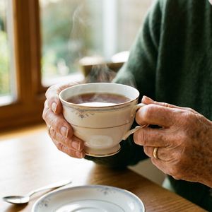 Nano Banana 2 output for the prompt: A 35mm film photo of an elderly woman's hands holding a steaming porcelain teacup, natural window light, Portra 400 grain