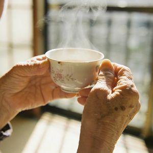 Seedream 4.5 output for the prompt: A 35mm film photo of an elderly woman's hands holding a steaming porcelain teacup, natural window light, Portra 400 grain