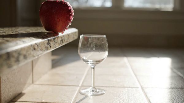 Google Veo 3.1 Lite output for the prompt: A ripe red apple falls from a kitchen countertop and shatters a wine glass on the tile floor below. Shards scatter, juice splashes. 24fps, natural morning light.