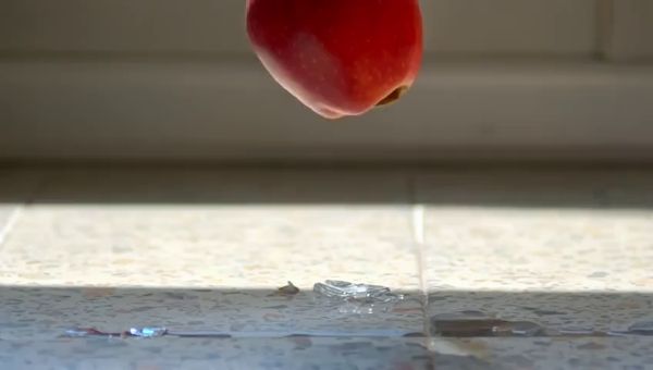 Mochi output for the prompt: A ripe red apple falls from a kitchen countertop and shatters a wine glass on the tile floor below. Shards scatter, juice splashes. 24fps, natural morning light.
