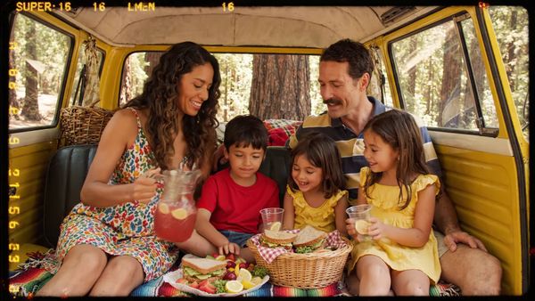 Google Veo 3.1 Lite output for the prompt: Super 16mm film grain, Kodachrome color: a family of four having a picnic in a yellow VW bus parked by a redwood forest. Children laughing, mom pouring lemonade.