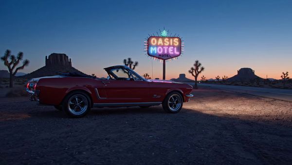 Google Veo 3.1 Lite output for the prompt: Slow orbit around a 1965 Mustang convertible parked on a Nevada desert highway at twilight. Neon motel sign blinking in the background. Cinematic widescreen.