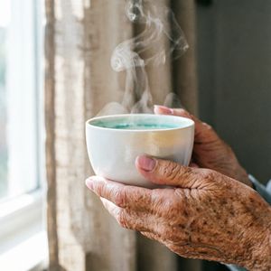 Qwen Image 2 output for the prompt: A 35mm film photo of an elderly woman's hands holding a steaming porcelain teacup, natural window light, Portra 400 grain