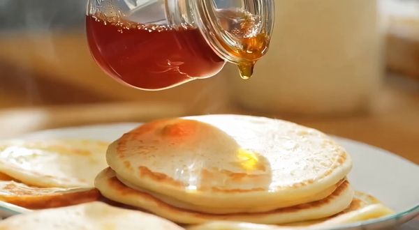 Wan v2.2 output for the prompt: A slow-motion close-up of honey being poured from a glass jar onto warm pancakes, light catching the viscous drip, steam rising subtly. Handheld, shallow depth of field.