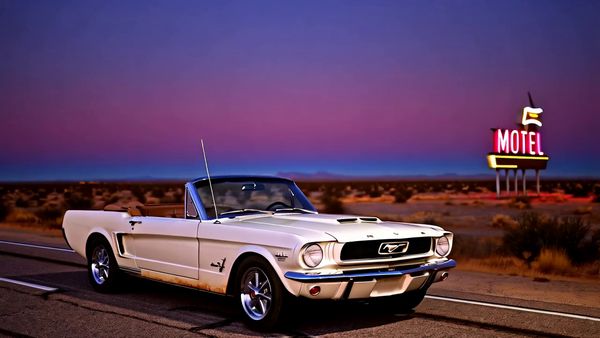 Minimax output for the prompt: Slow orbit around a 1965 Mustang convertible parked on a Nevada desert highway at twilight. Neon motel sign blinking in the background. Cinematic widescreen.