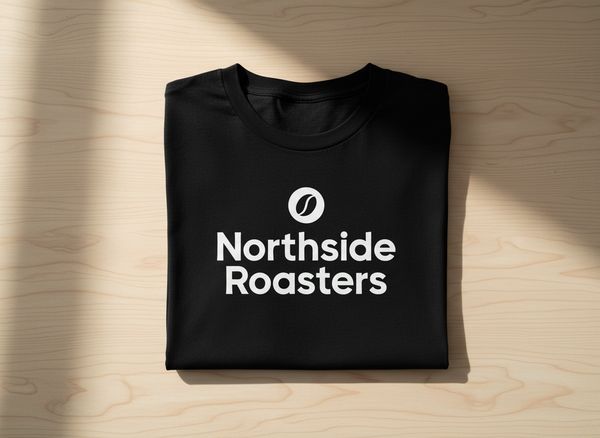 Black cotton t-shirt folded on a light wooden table, logo printed in white on the chest, soft natural light, top view.