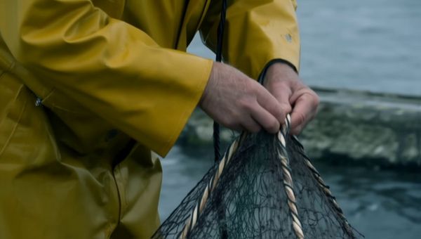 Luma Ray 2 output for the prompt: A elderly Japanese fisherman in a yellow raincoat mends a net on the dock. Cut to the same fisherman walking up a stone path toward a lighthouse, seen from behind. Overcast sky, 35mm film look.